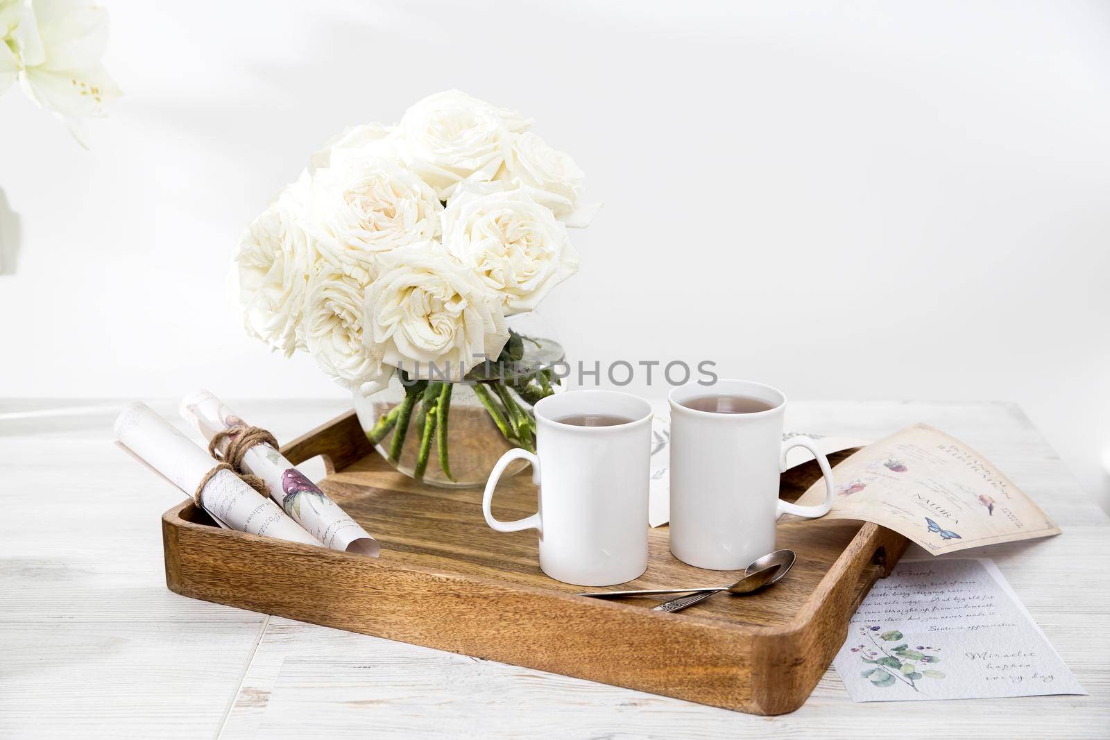 A bouquet of white roses in a glass vase on a tray with two cups of coffee, a kettle, and a milk jug. Copy space by elenarostunova