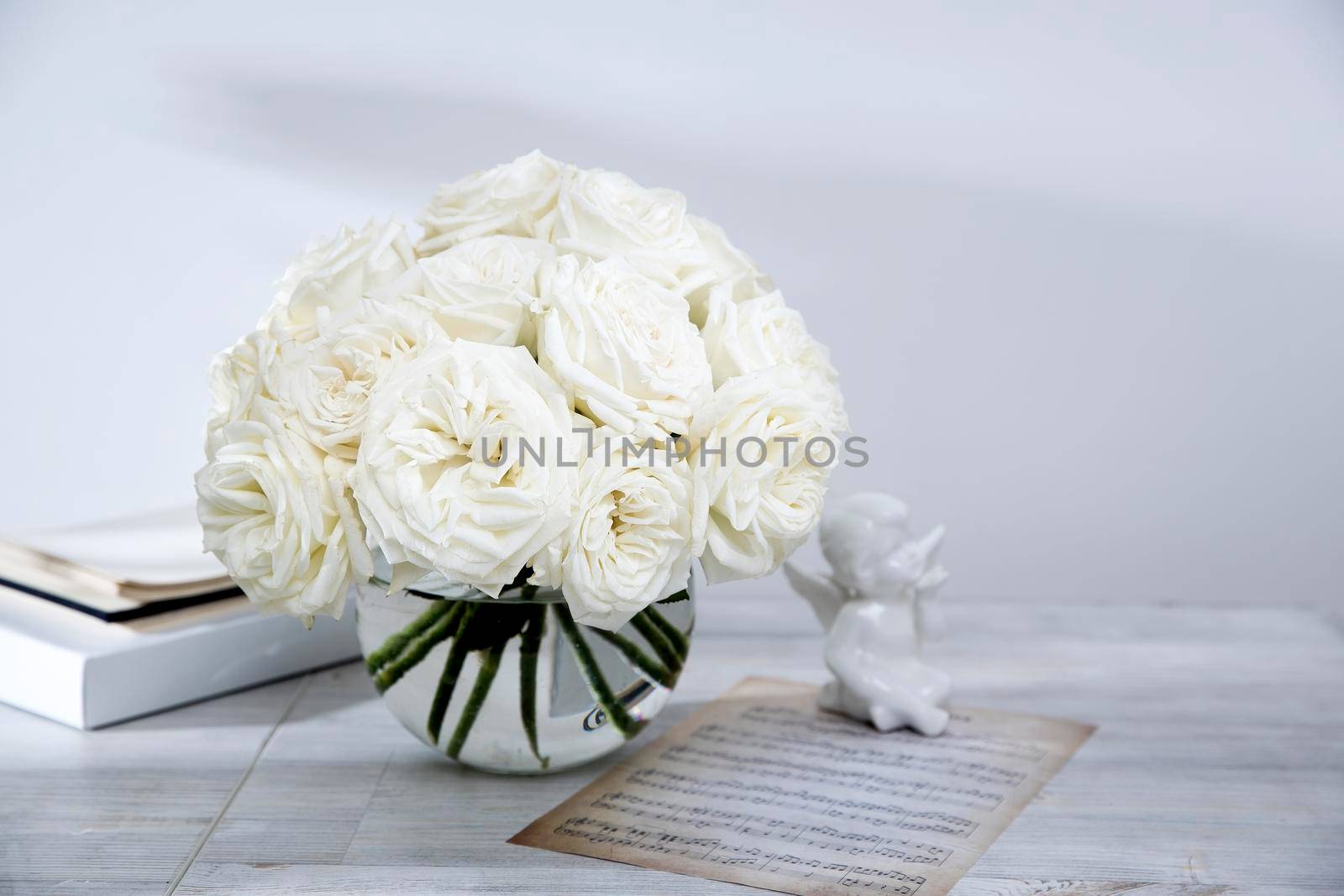 A bouquet of white roses in a round glass vase on a table with a cup of tea and a book. Copy space. Figurine of pears by elenarostunova