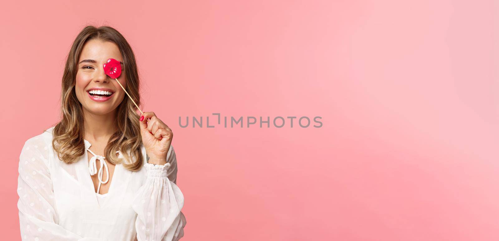 Spring, happiness and celebration concept. Close-up portrait of funny and carefree young beautiful blond girl having fun at party with girlfriends, holding lips stick and laughing, pink background by Benzoix