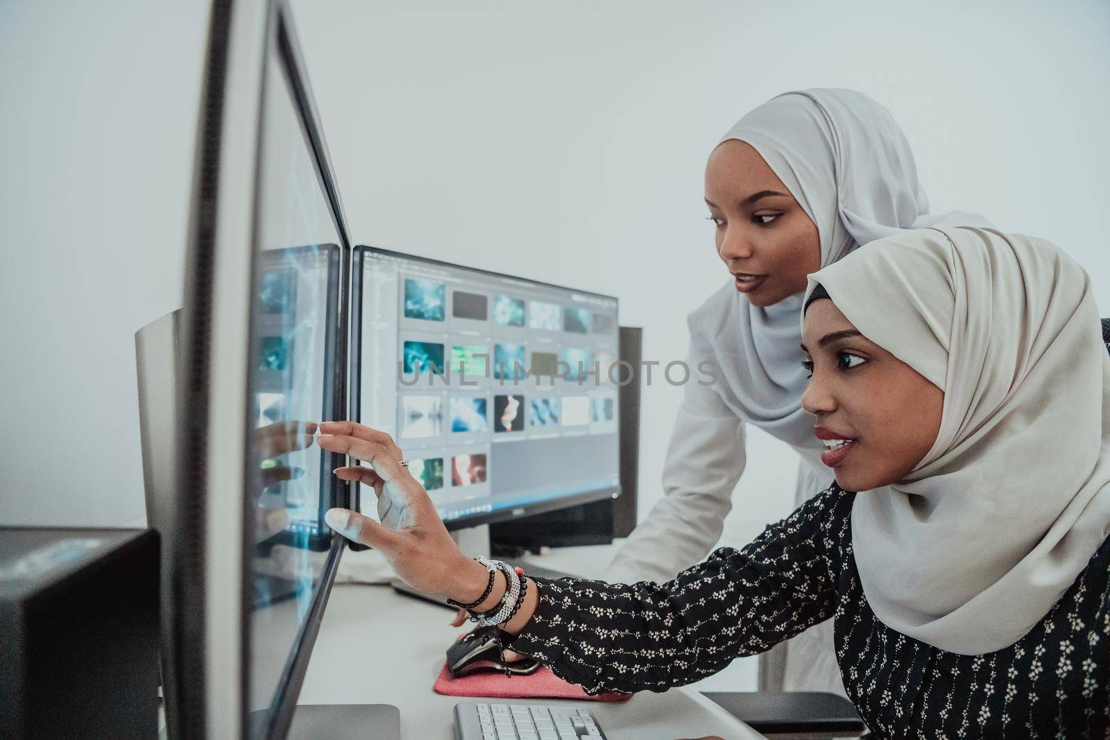 Friends at the office two young Afro American modern Muslim businesswomen wearing scarf in creative bright office workplace with a big screen by dotshock