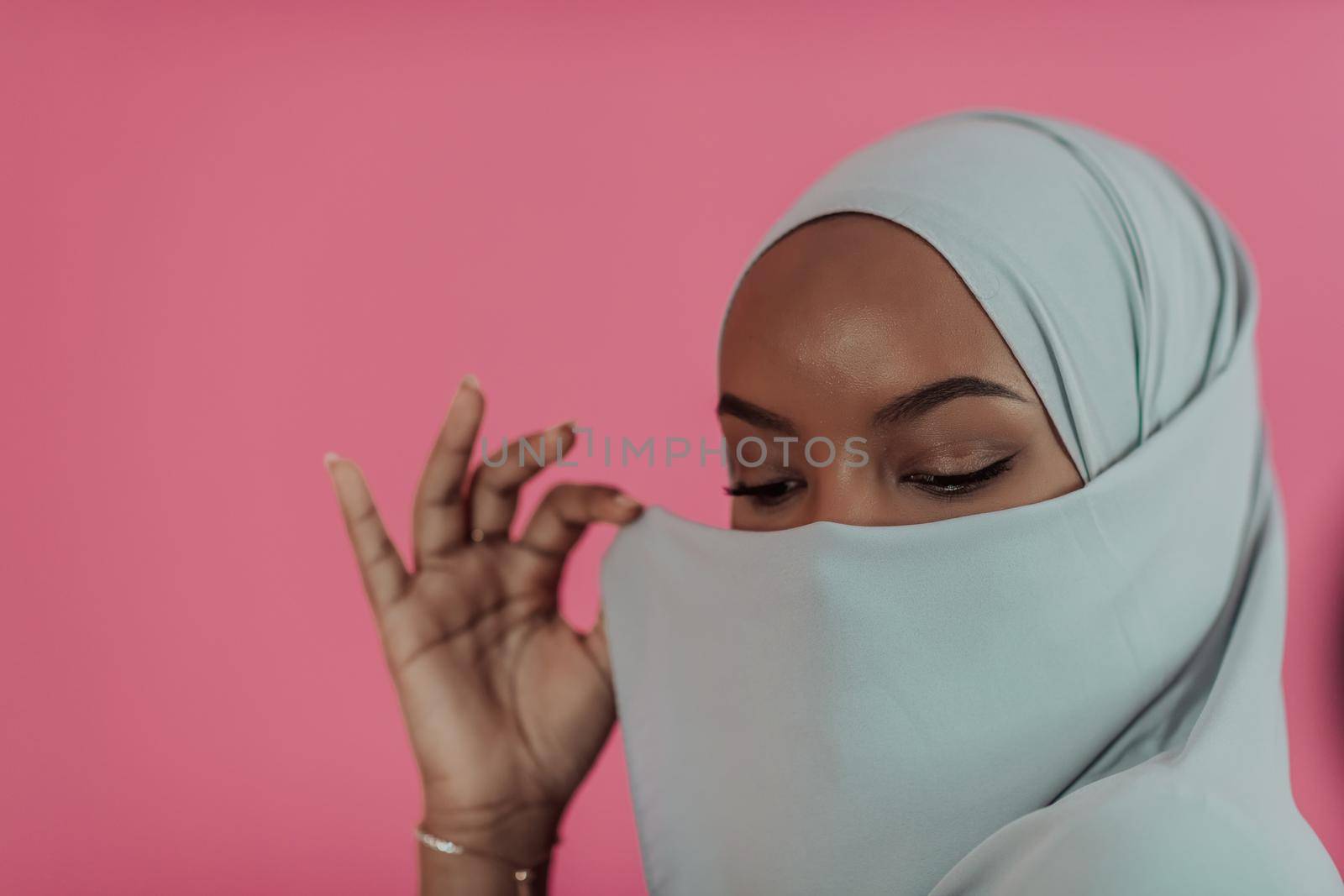 Portrait of young modern muslim afro beauty wearing traditional islamic clothes on plastic pink background. Selective focus by dotshock