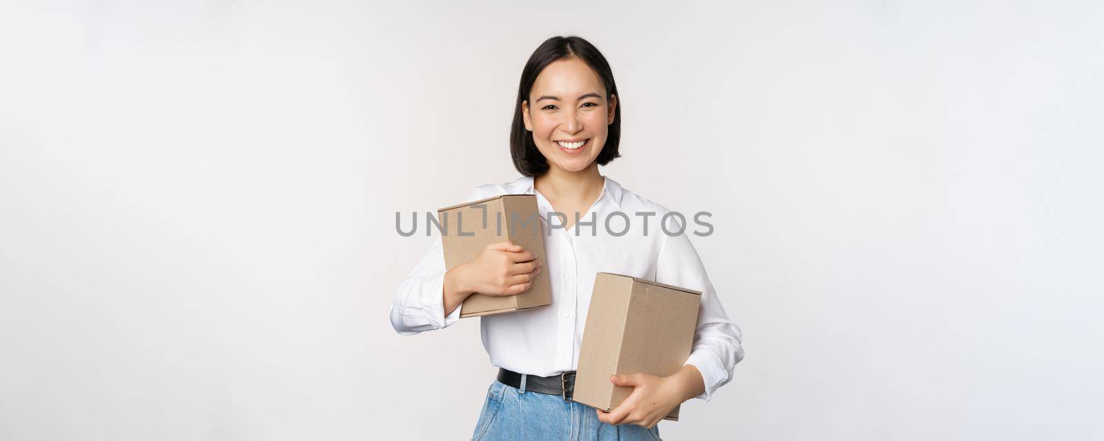 Concept of shopping and delivery. Young happy asian woman posing with boxes and smiling, standing over white background.