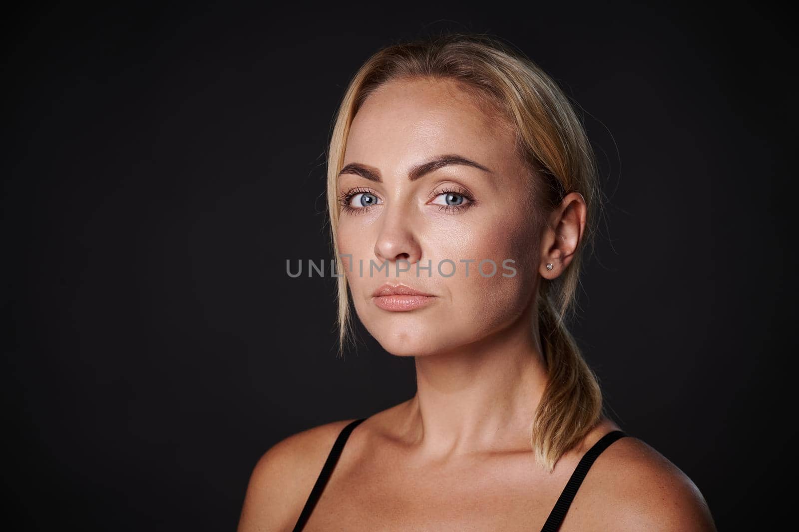 Beautiful gorgeous 30s young Caucasian blonde woman looking at camera isolated on black. Close-up beauty portrait. Healthy skin, body care, beauty treatment, cosmetology concept