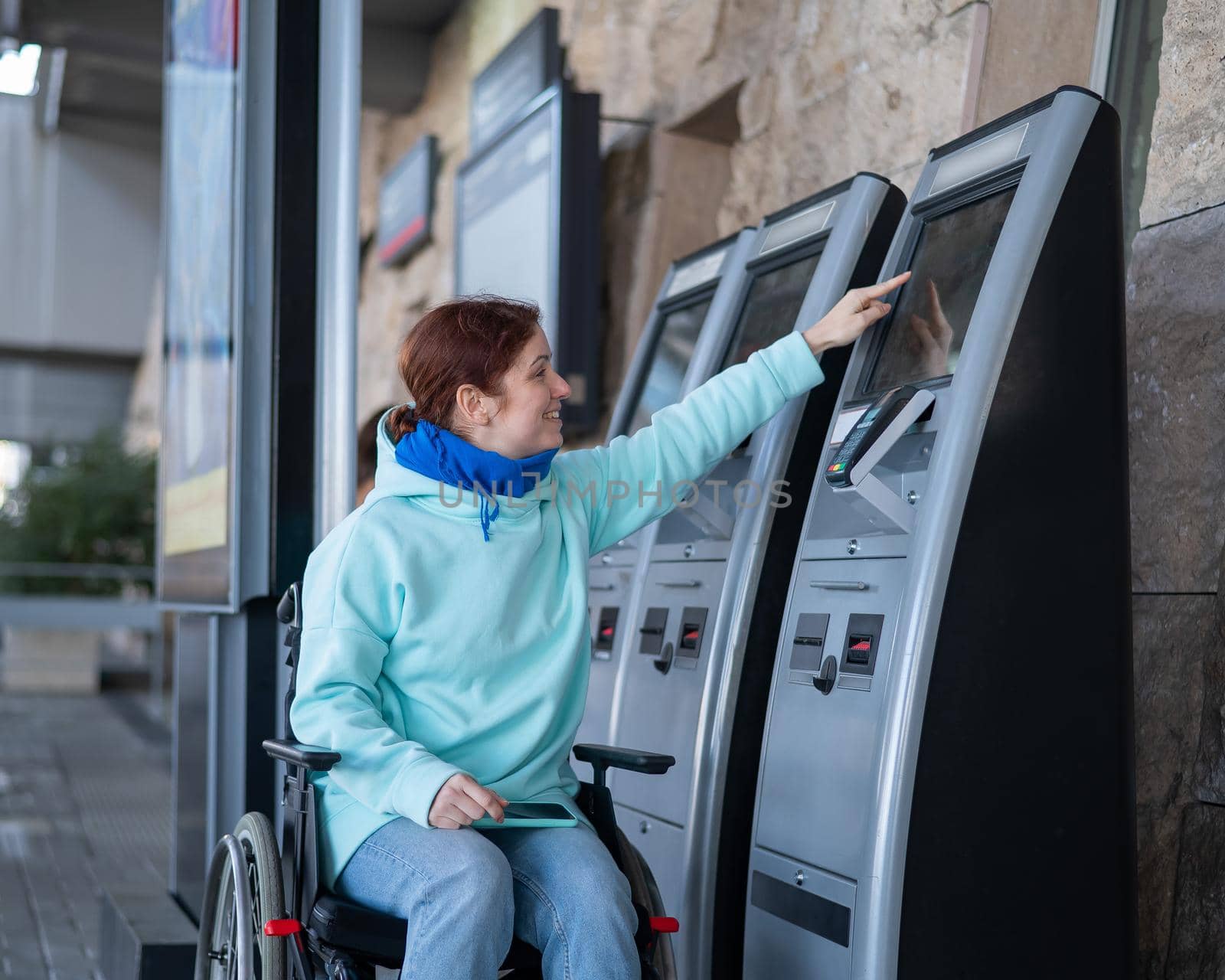 Caucasian woman in a wheelchair buys a train ticket at a self-service checkout. by mrwed54