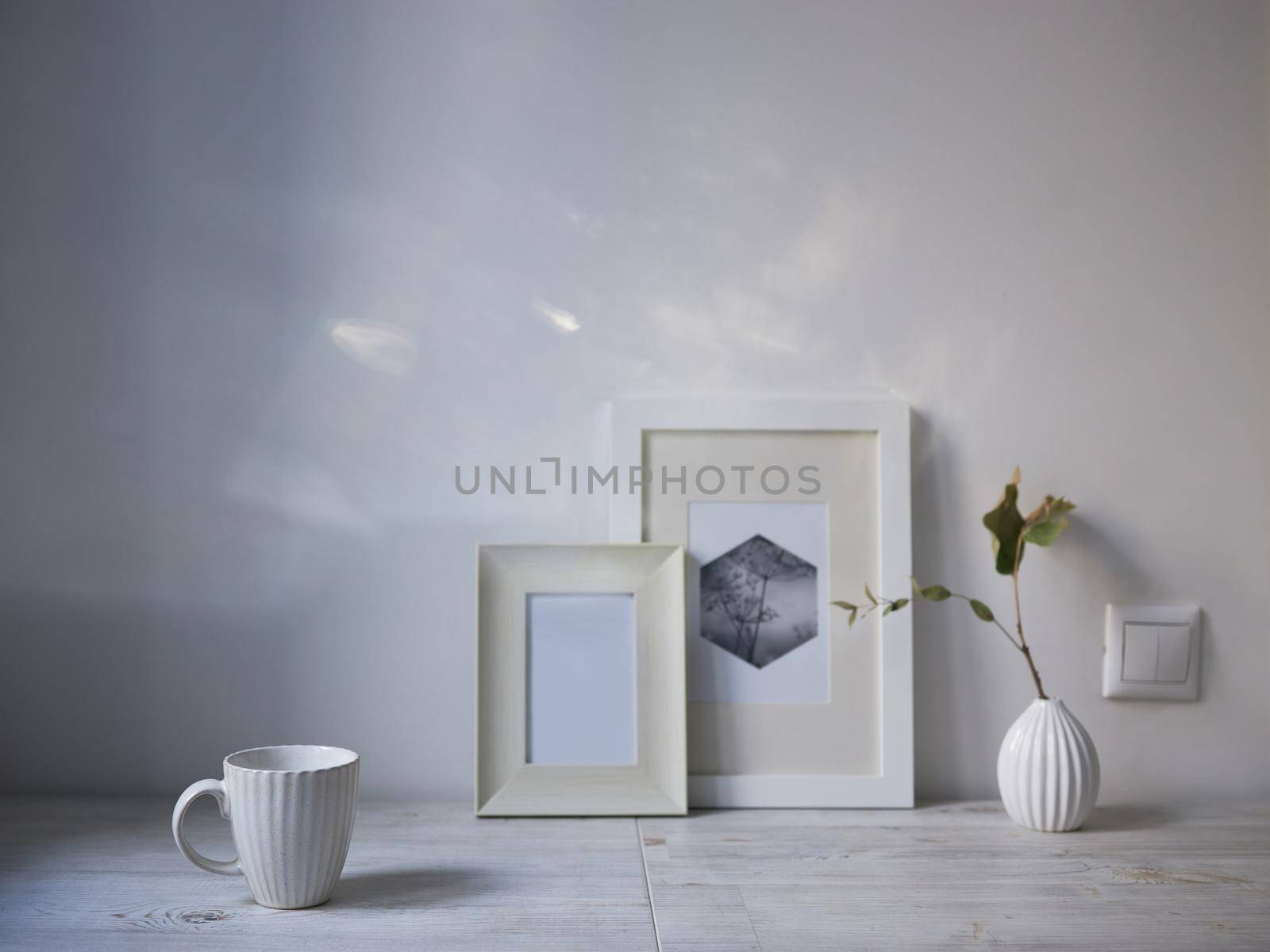 Scandinavian style. Interior Design. A white cup, a small vase with a dried eucalyptus branch, a two photo frames are on the table. Copy space for text