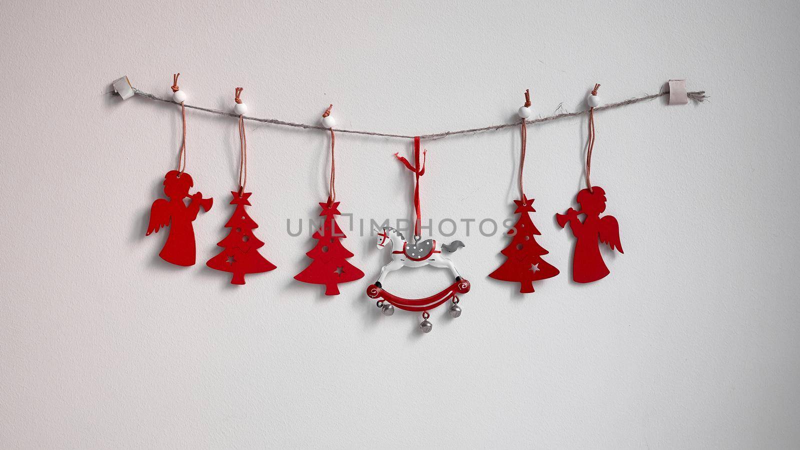 Christmas composition. A garland of red wooden toy fir trees and a rolling horse on a rough rope on a white background. Christmas, winter, new year concept. Flat, top view, copy space by elenarostunova