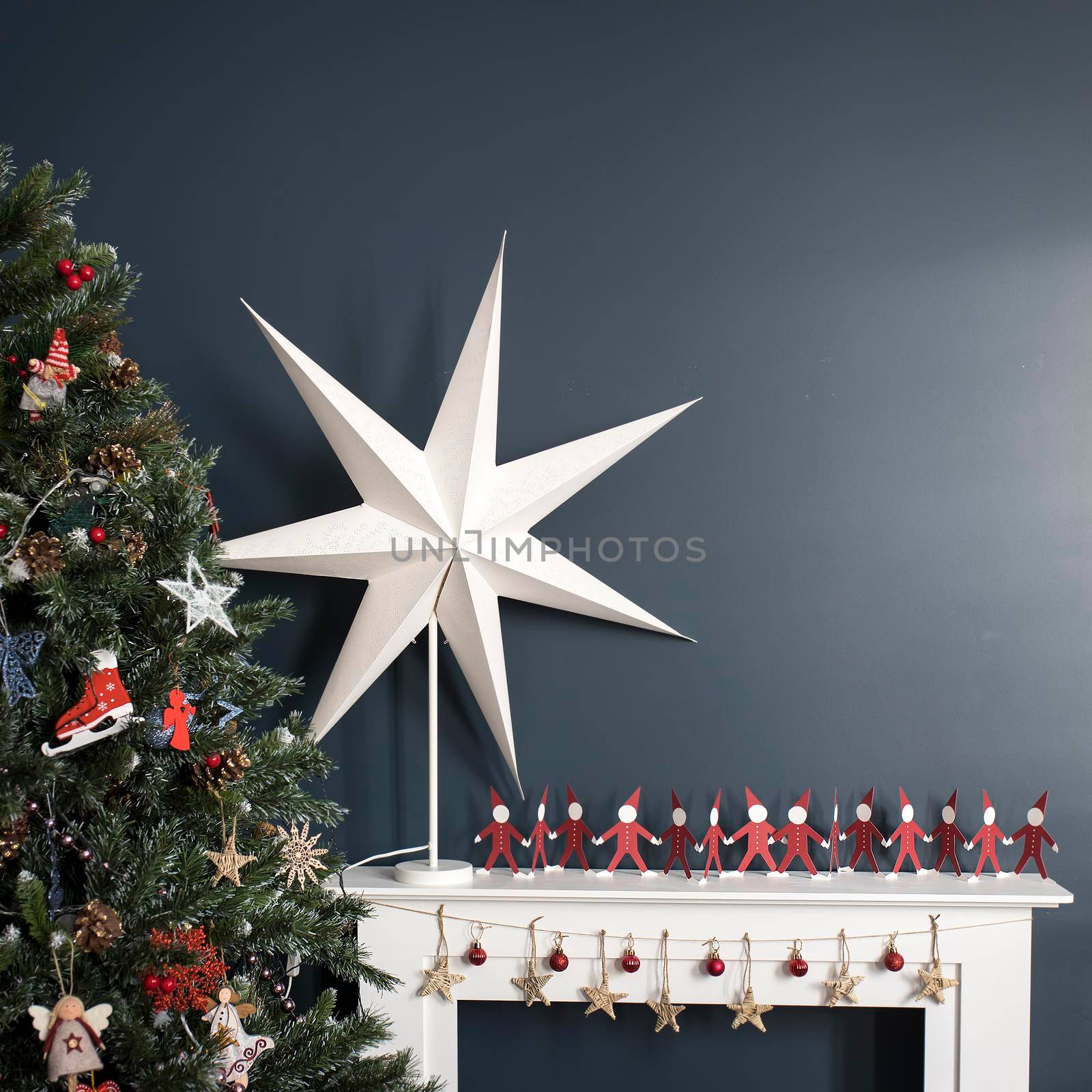 Red paper men holding hands on white and a large paper star on the background of tree there is an artificial fireplace on the background of a dark blue wall as an interior decoration for Christmas