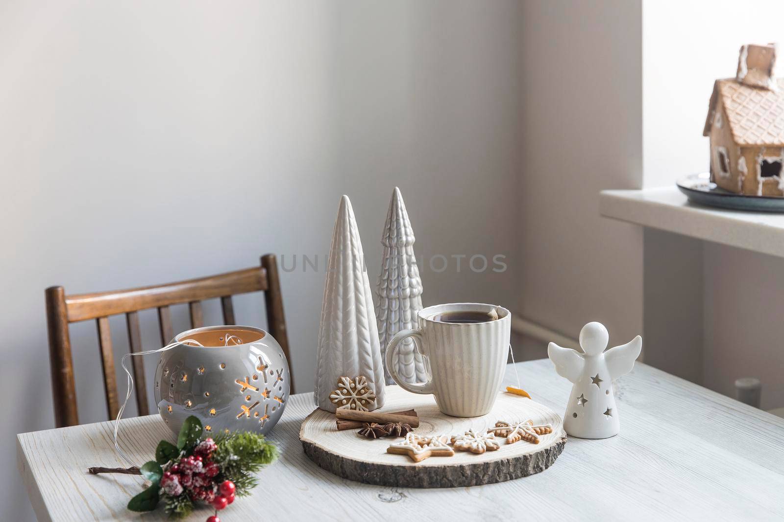 A cup of coffee on a wooden stand, ceramic Christmas trees in pastel colors, gingerbread cookies, gray candlestick. Artificial spruce branch with red berries. Scandinavian style. Copy space.