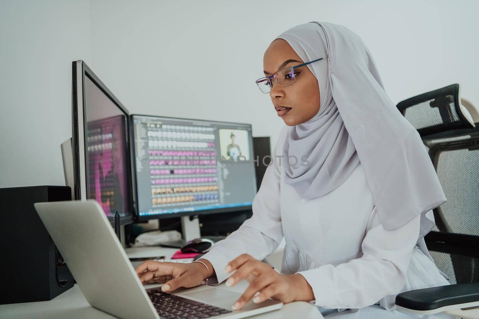 Young Afro-American modern Muslim businesswoman wearing a scarf in a creative bright office workplace with a big screen. by dotshock