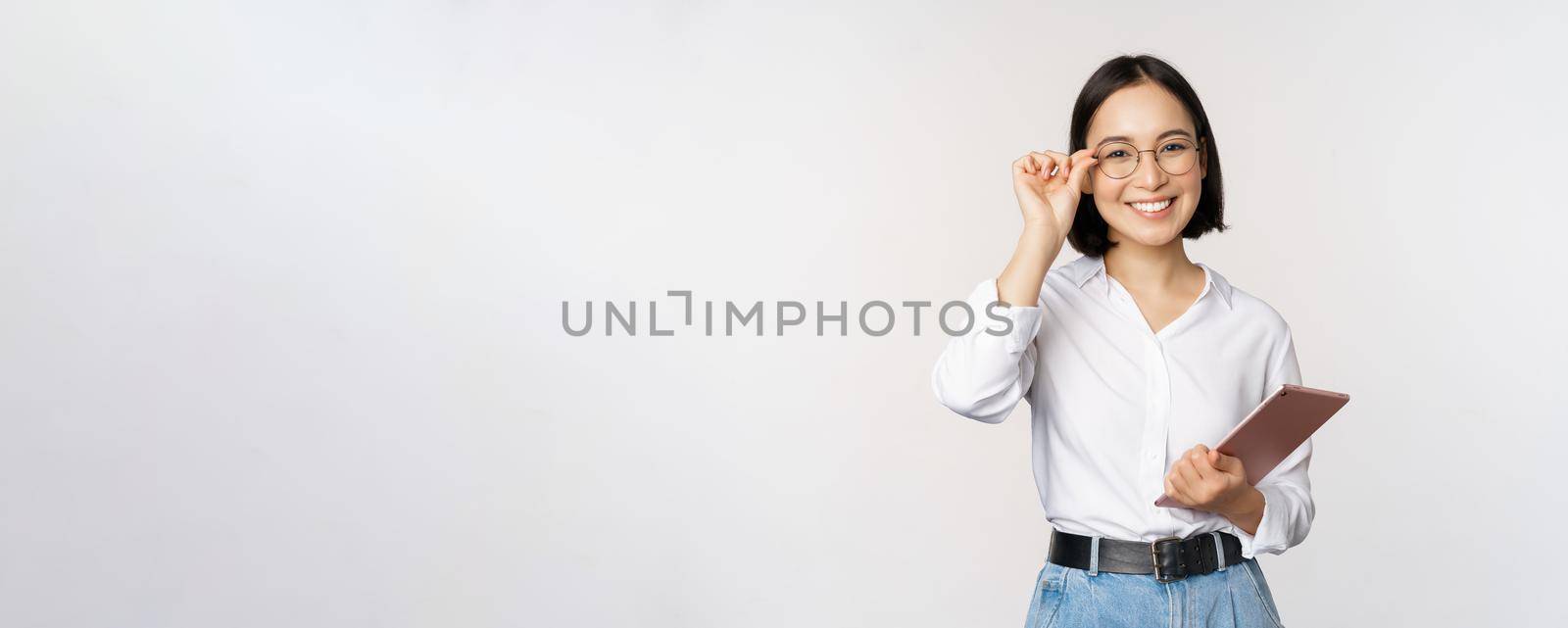 Image of young asian business woman, female entrepreneur in glasses, holding tablet and looking professional in glasses, white background.