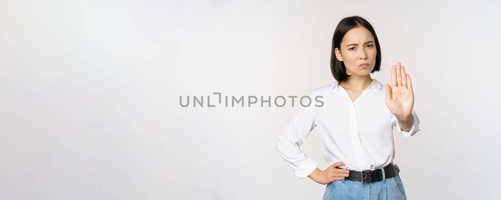 Portrait of young woman extending one hand, stop taboo sign, rejecting, declining something, standing over white background. Copy space