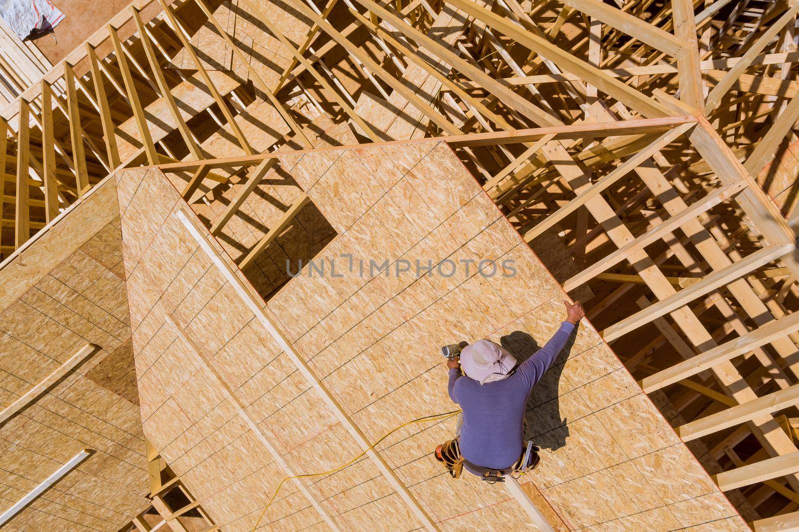 Carpenter with nailing plywood on roof of in unfinished house