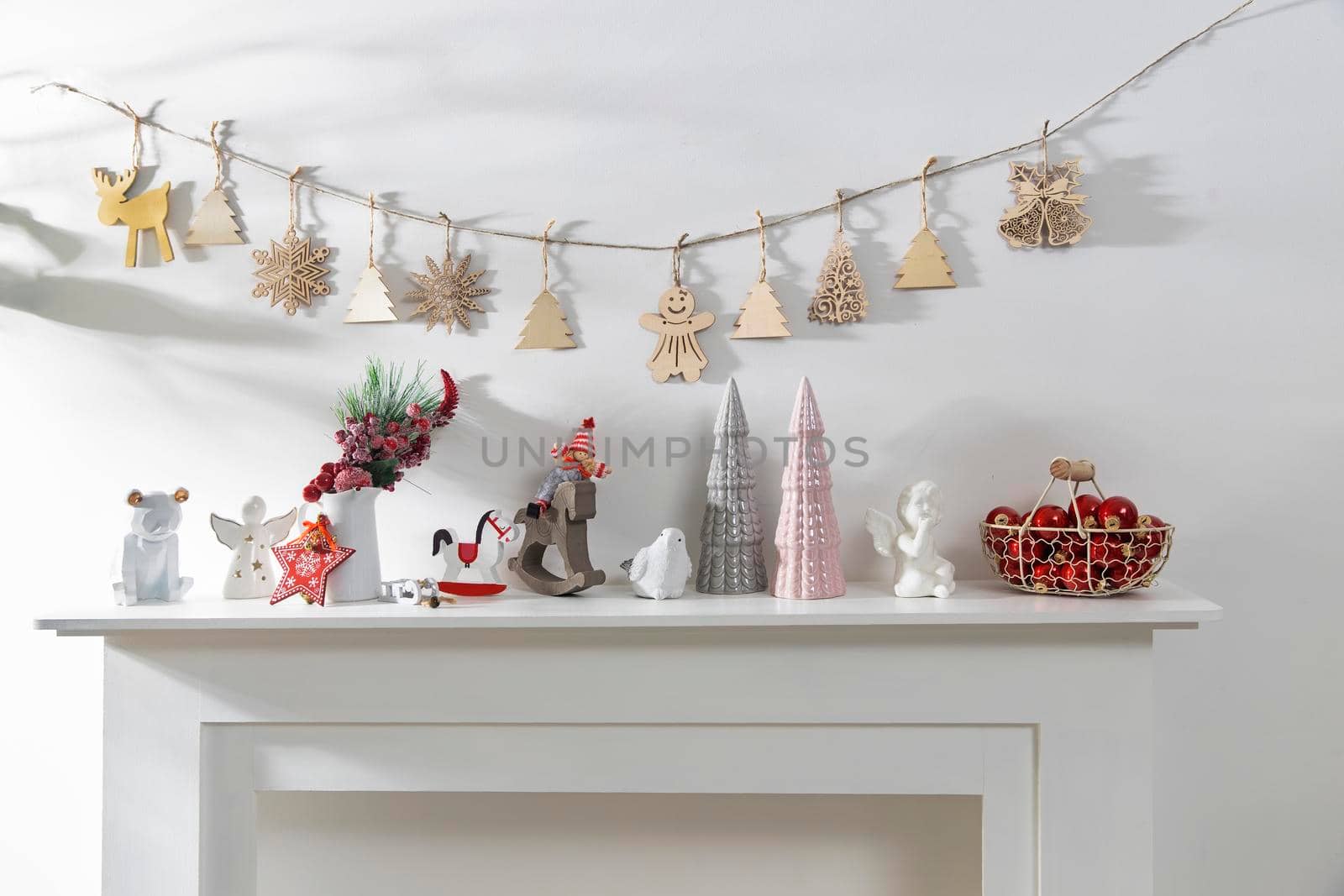 Decoration of the interior of the apartment for Christmas. A garland of carved wood figures. Candles and ceramic figurines on a fake fireplace. Copy space.