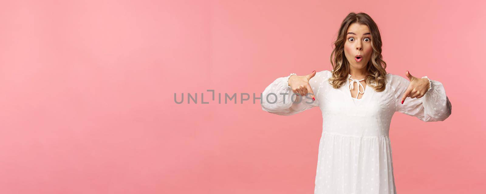 Waist-up portrait of interested, excited attractive blond 20s woman showing person something really cool, say wow pop eyes camera excited, pointing fingers down at great offer, pink background by Benzoix