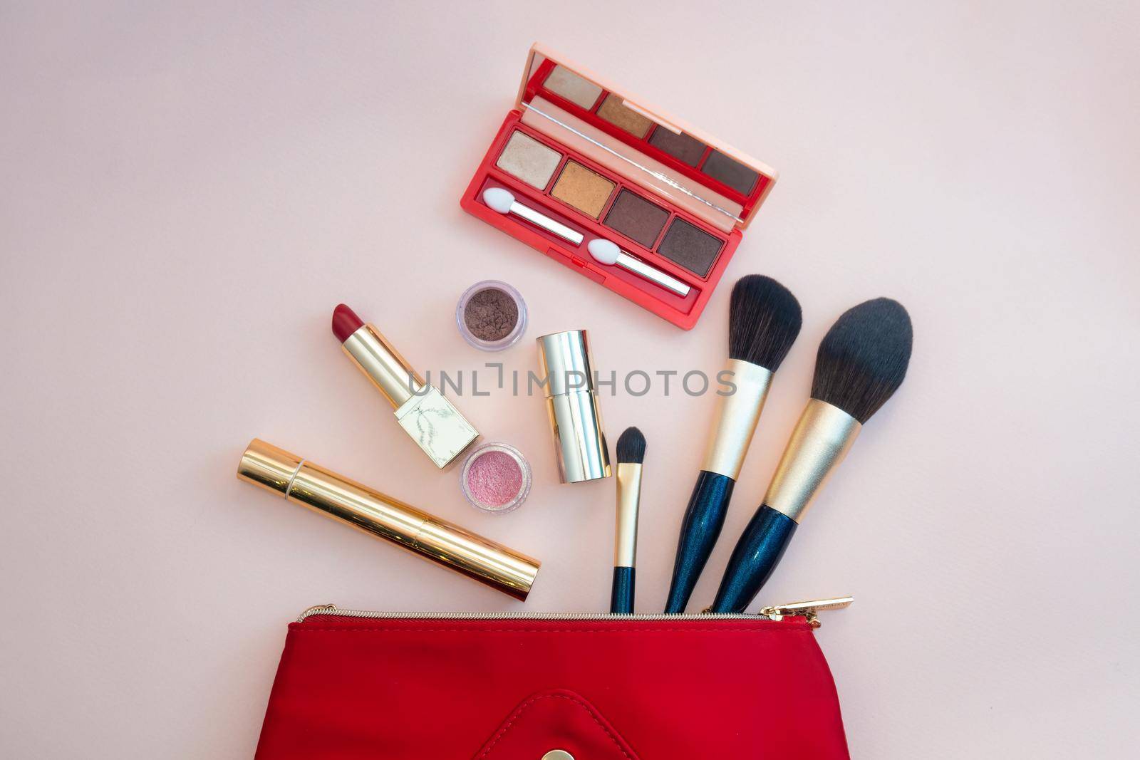 Top view of cosmetics standing out from red cosmetic bag on pink background. Photo