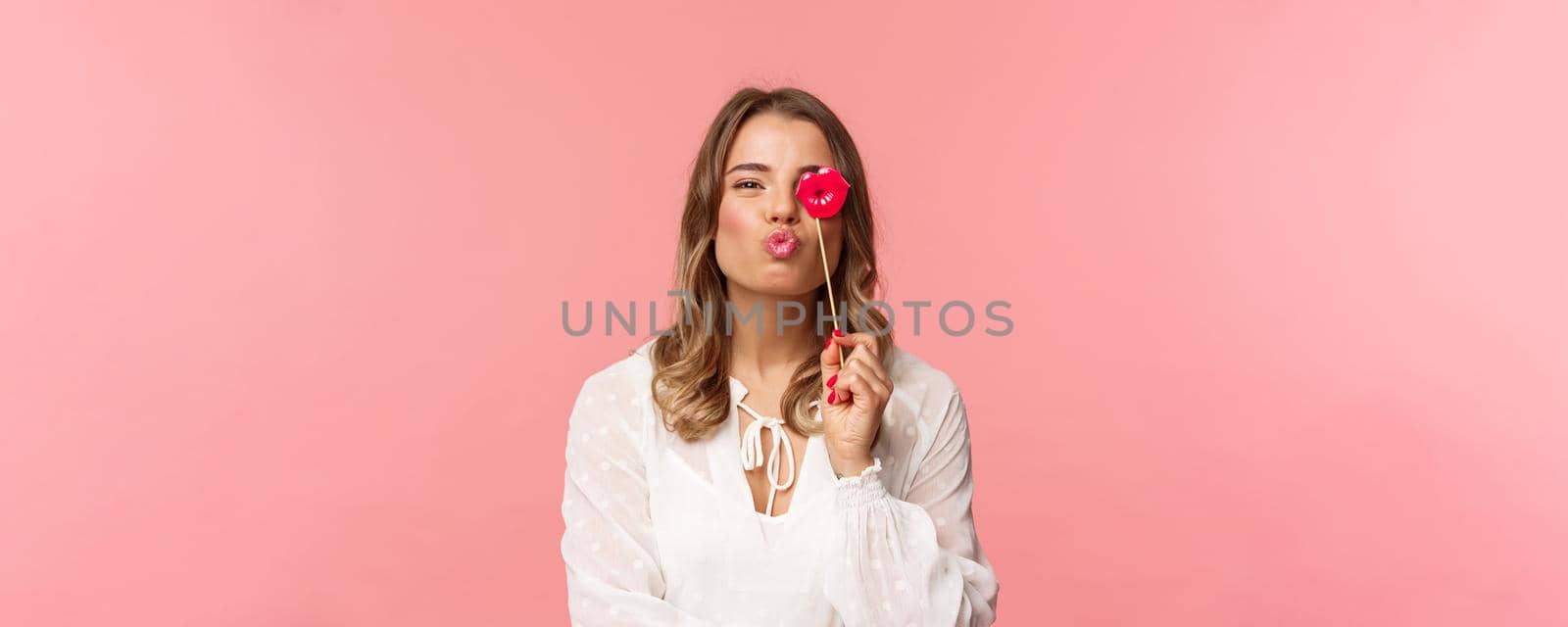 Spring, happiness and celebration concept. Close-up portrait of feminine lovely blond girl in white dress, folding lips in kiss and holding carton stick, partying having fun, stand pink background by Benzoix
