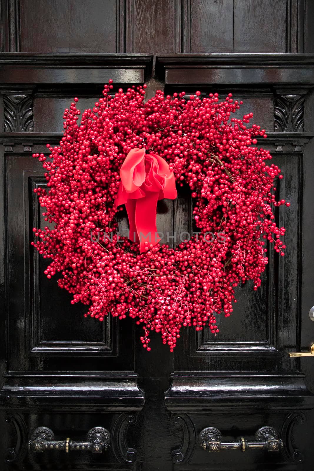 A red wreath collected from hawthorn berries and branches hangs on the black door. Christmas decoration by elenarostunova