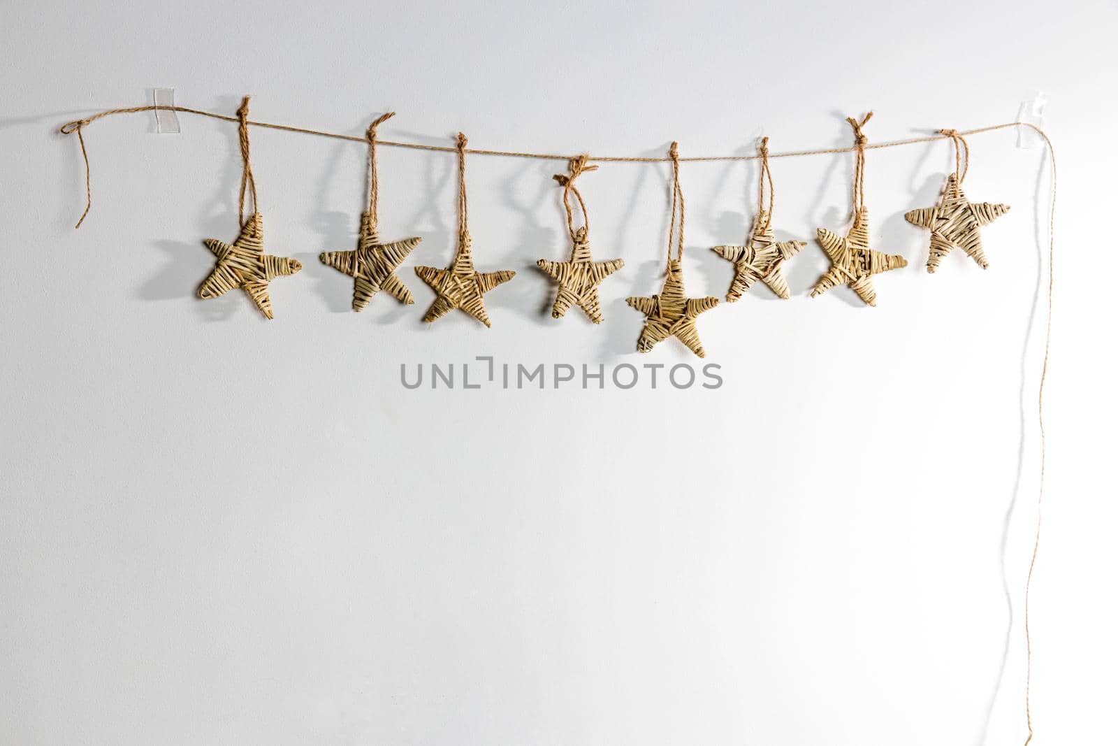 A handmade garland of braided stars is on a white wall. Place for text. Copy space