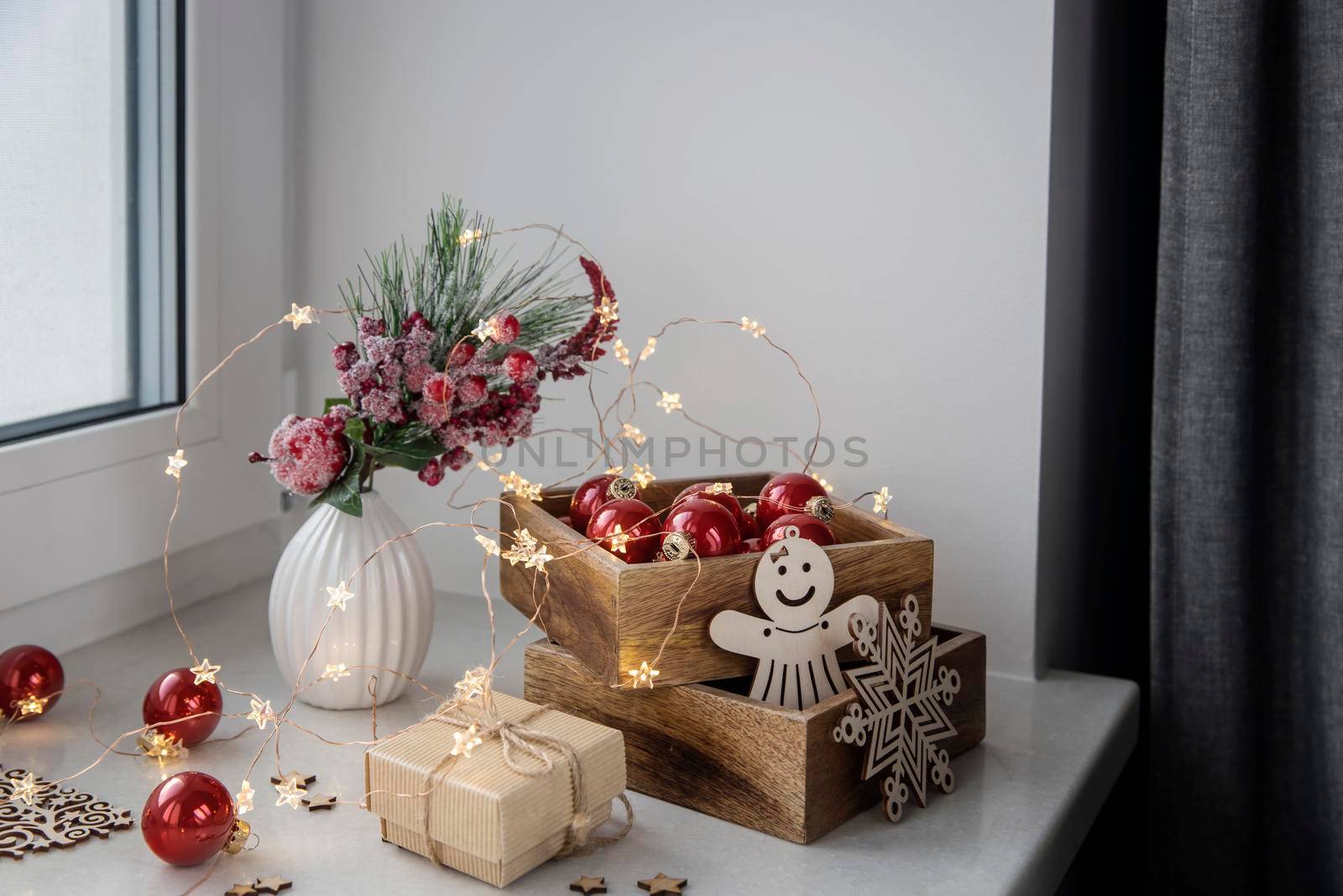 An artificial spruce branch, decorated with ivy leaves, apples and hawthorn berries. Lighted candles in wooden box, red glass balls, winter composition decorates interior on eve of Christmas by elenarostunova