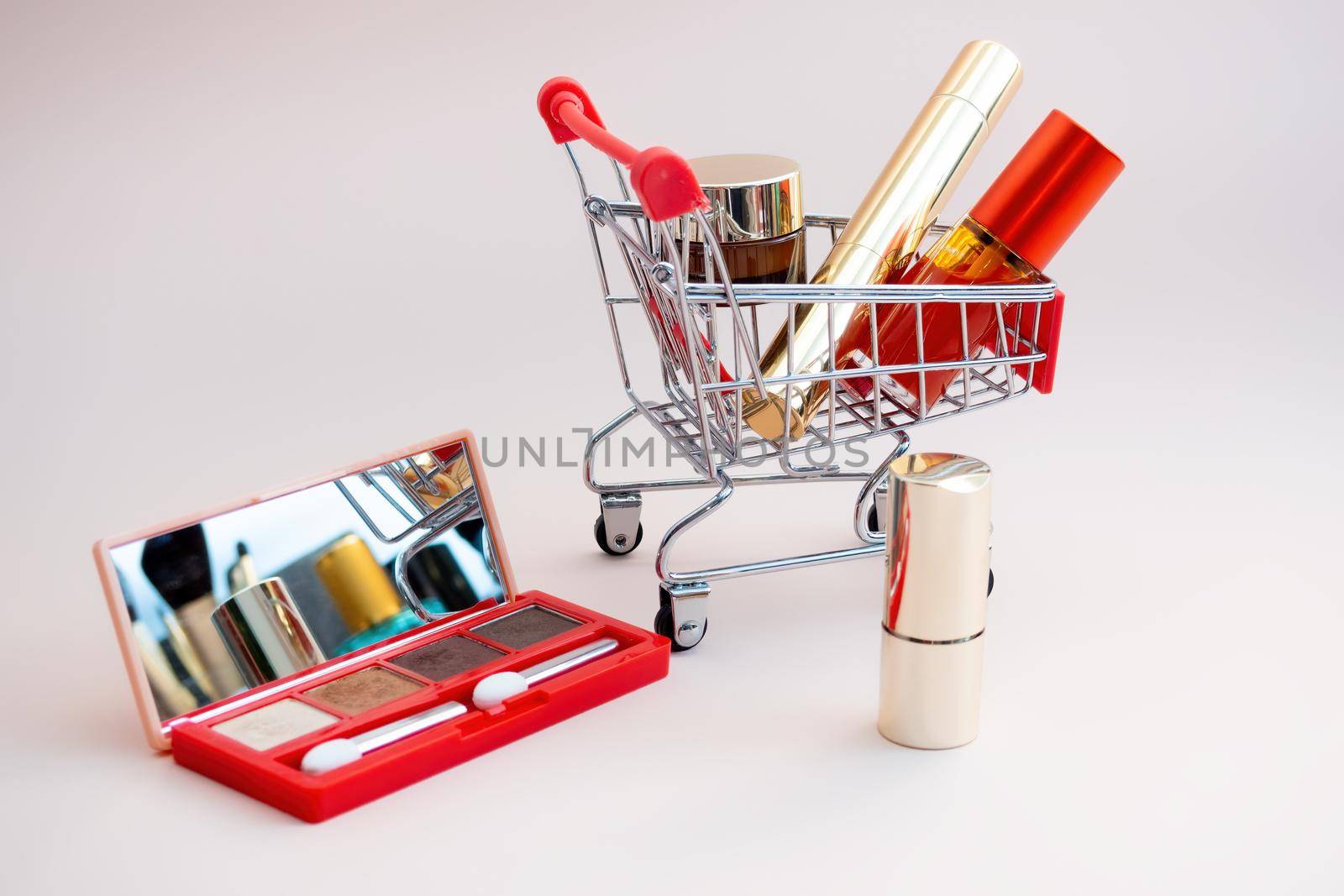 Front view of a shopping cart with makeup products on a pink background. Cosmetic shopping concept. photo