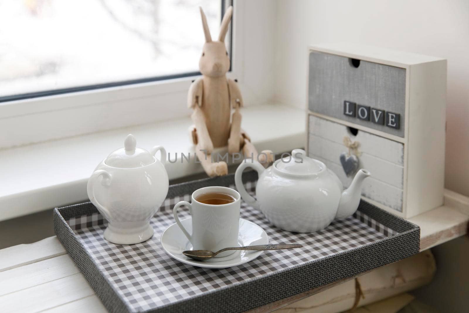Tea drinking. A cup of tea, a sugar bowl and a kettle are on the tray. A small wooden chest of drawers with two drawers and the inscription "Love", there is a wooden hare on hinges by the window by elenarostunova