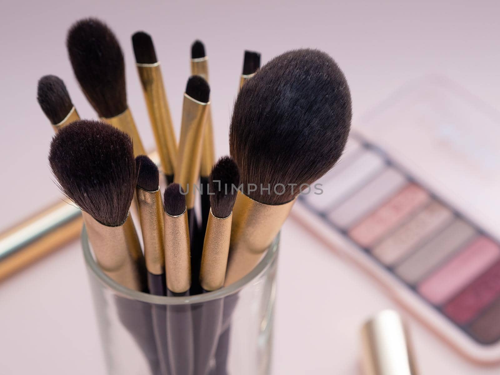 Composition with decorative makeup products golden brushes and colorful eye shadows on pastel pink background. photo