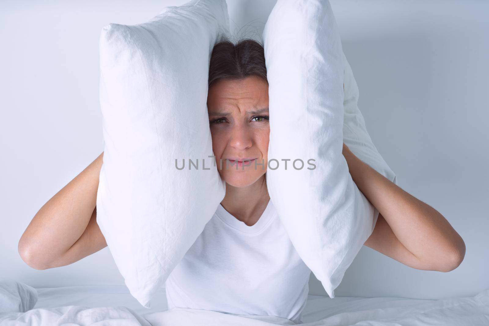 Young woman disturbed by noisy neighbours. Woman struggling from noise in bed and covering ears with pillows by DariaKulkova