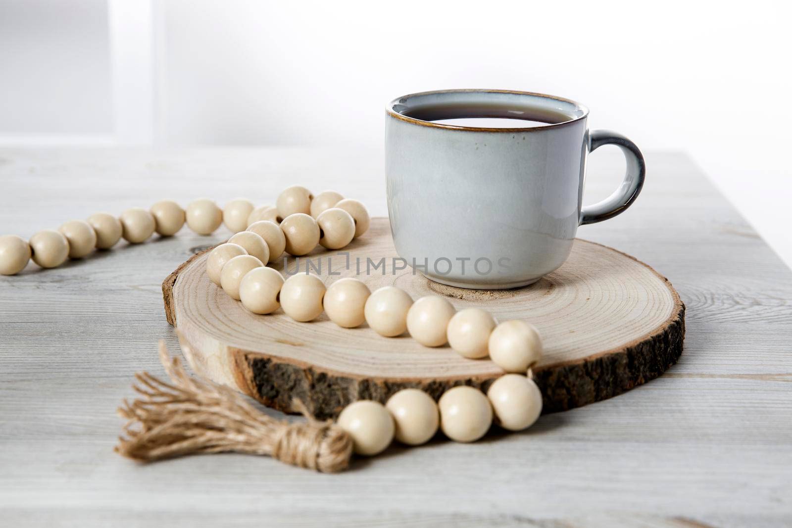 A blue ceramic cup on a wooden round cut, beads, a rosary for prayer on a beige table against a white wall. Place for text by elenarostunova