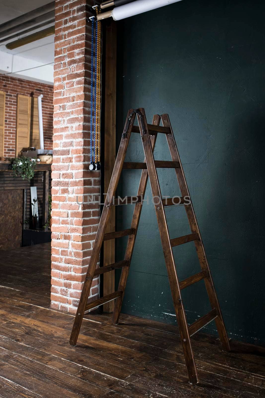 Wooden brown ladder stepladder on a wooden floor near a dark blue wall for installation work