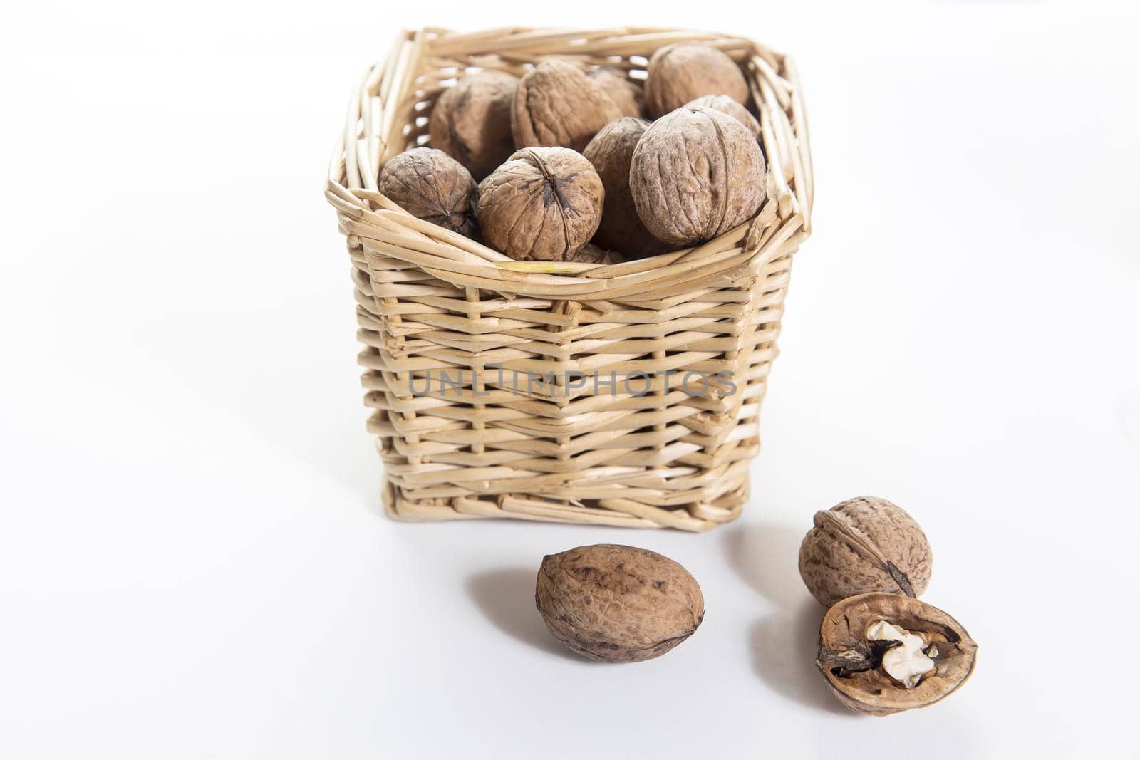 Walnuts are sprinkled in a yellow wicker willow basket isolated on white. Place for your text. Copy space by elenarostunova