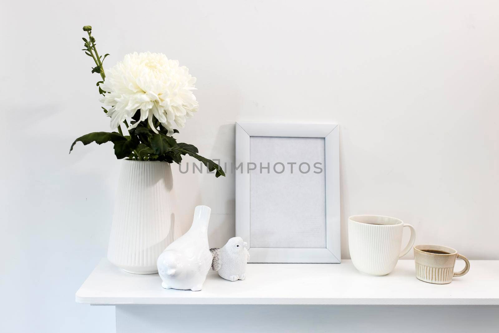 Large chrysanthemum in a glass vase. Photo frame with place for text, two corrugated cups with coffee and ceramic figurines of birds on the table. Office decoration. Copy space