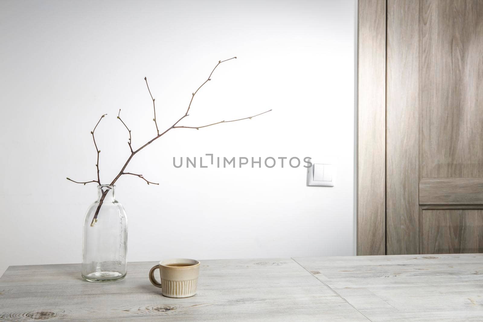 An unblown linden branch are in a glass vase and a small beige cup of coffee on the table. Scandinavian style. Place for your text by elenarostunova