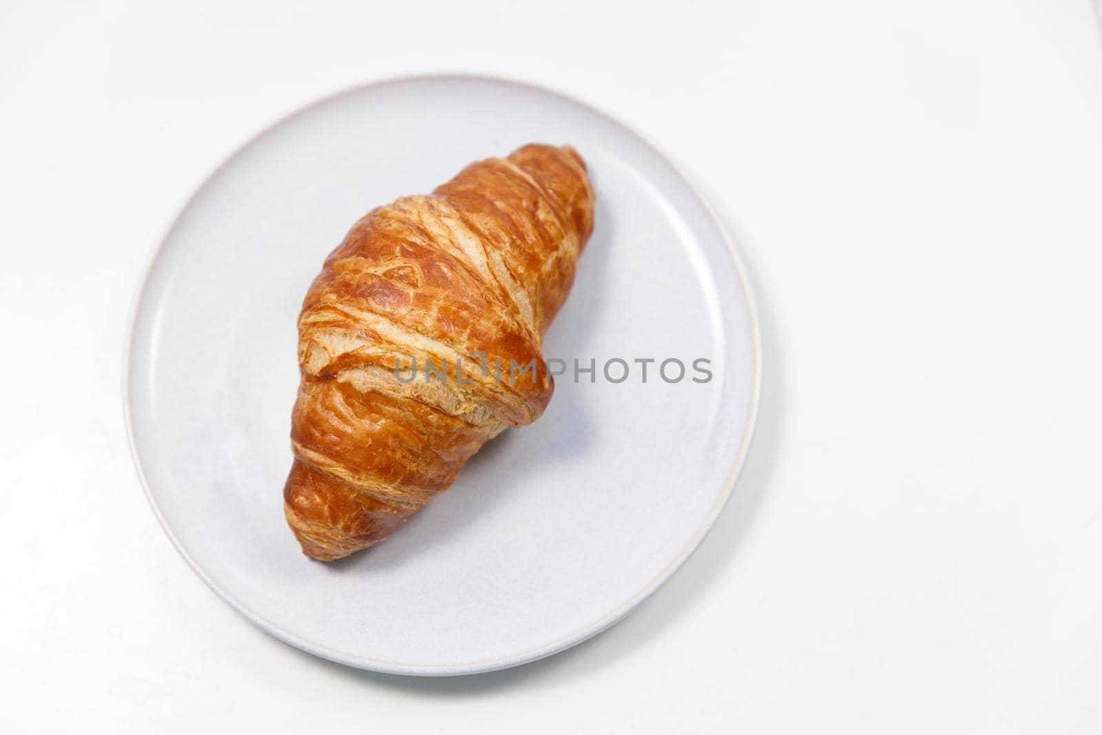 Freshly baked croissant on gray round plate on white background by elenarostunova