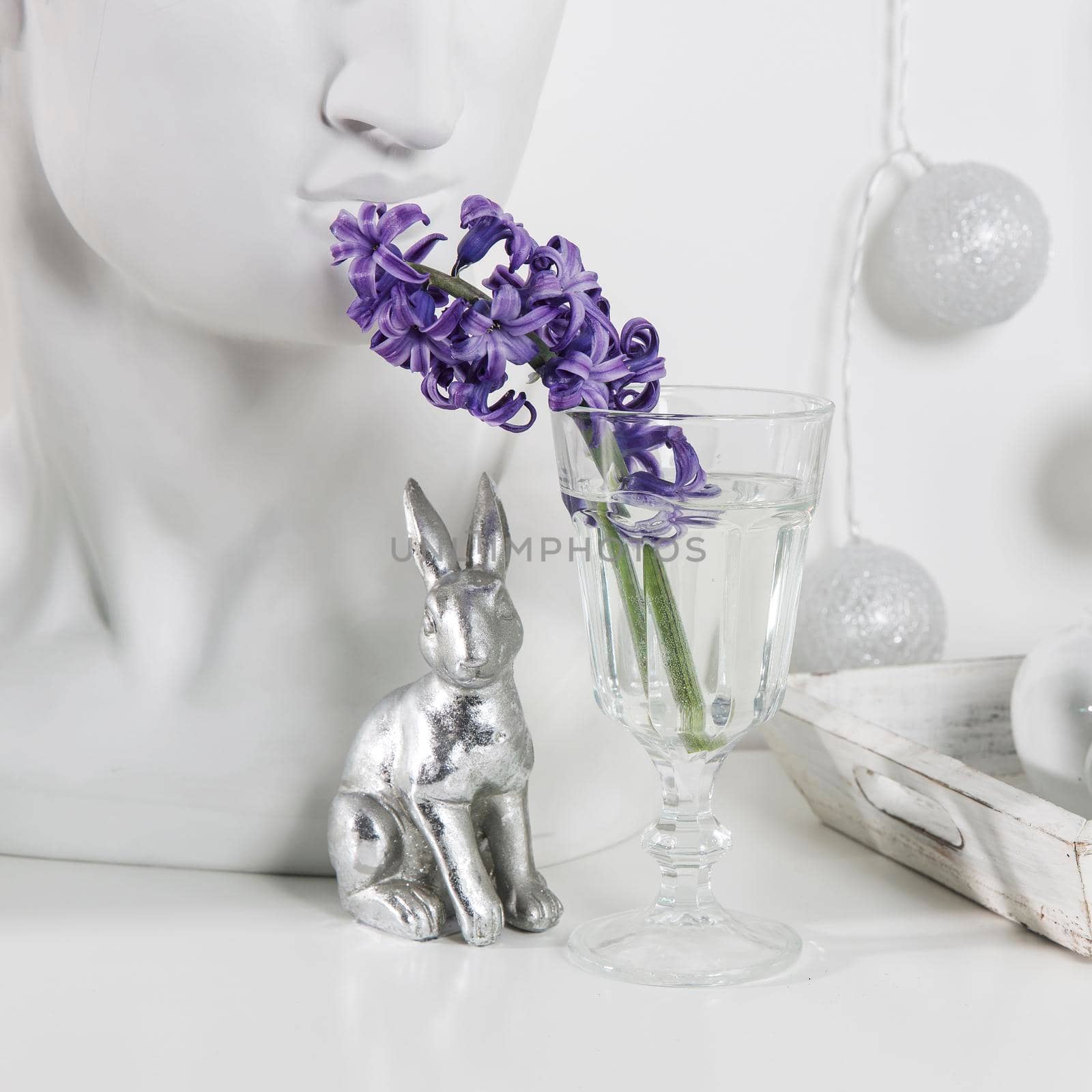 Ceramic figurines of Easter bunnies of different sizes on the table. Blue and white hyacinths in glass cups on a white background. Easter design
