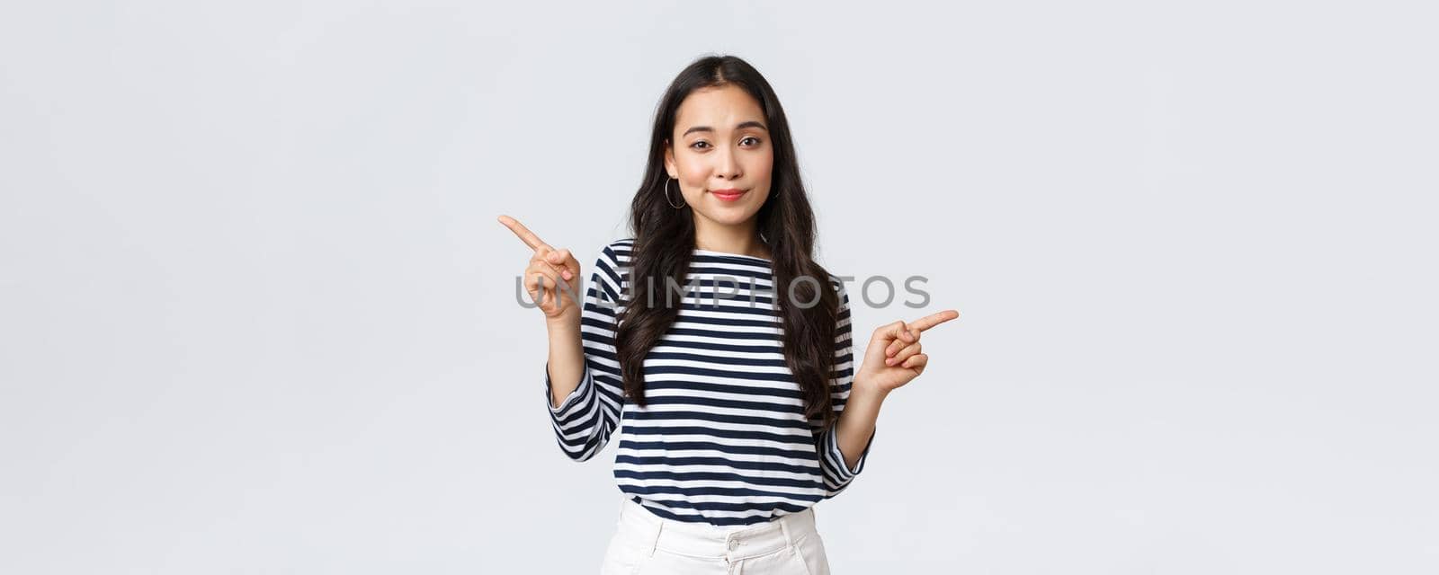 Lifestyle, beauty and fashion, people emotions concept. Indecisive cute korean girl need help with choice, pointing fingers sideways, showing left and right products, making decision.