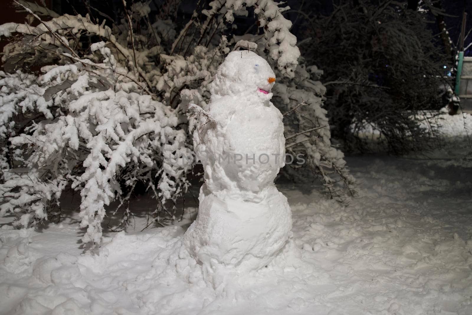 Snowman on the playground in the snowfall at night by elenarostunova