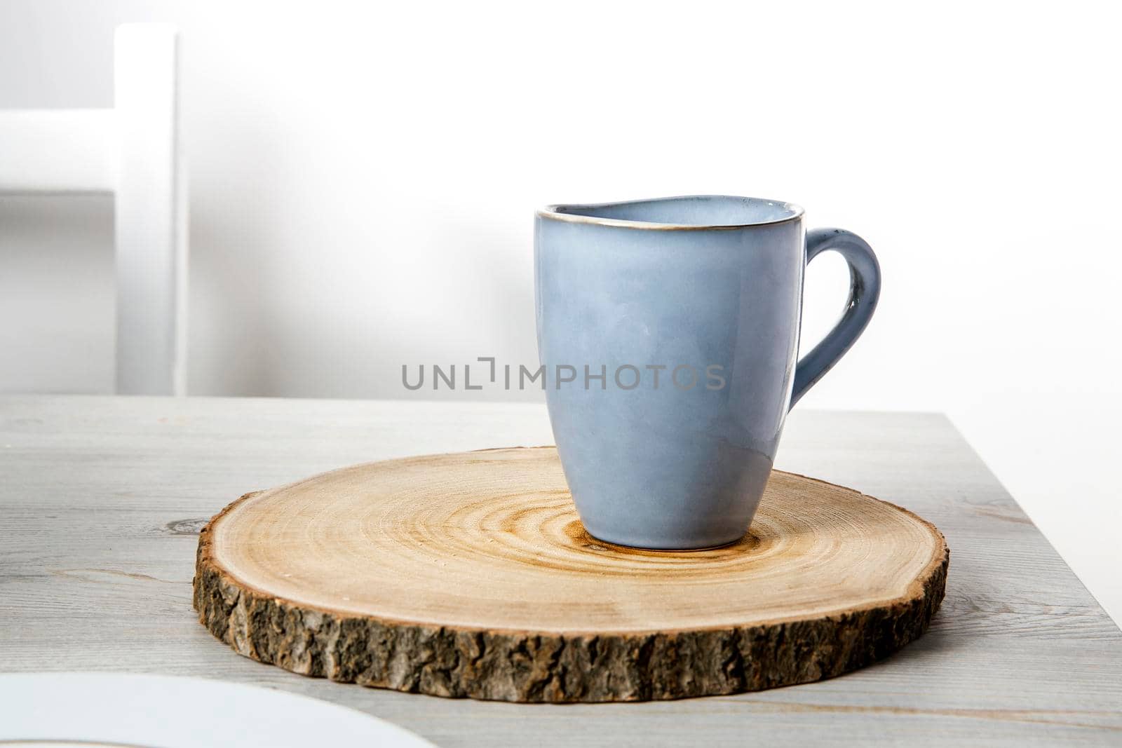 A blue ceramic cup on a wooden round cut on a beige table against a white wall. Place for text. Copy space by elenarostunova