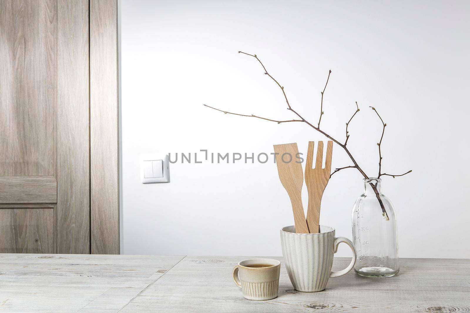 An unblown linden branch in a glass vase and a small beige cup with coffee and a cup with kitchen wooden utensils on the table. Scandinavian style. Place for your text