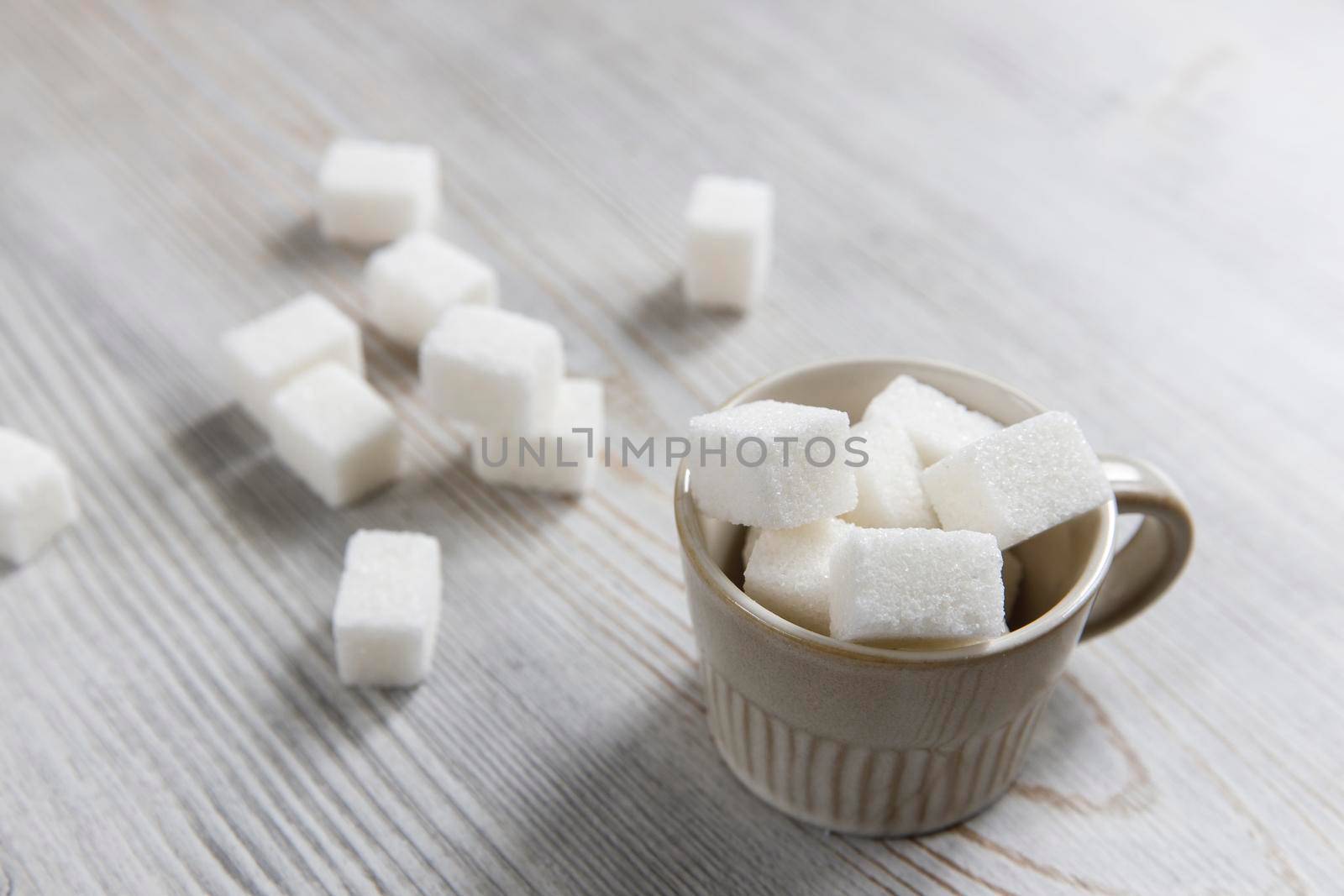 Cup with refined sugar in pieces scattered on the table