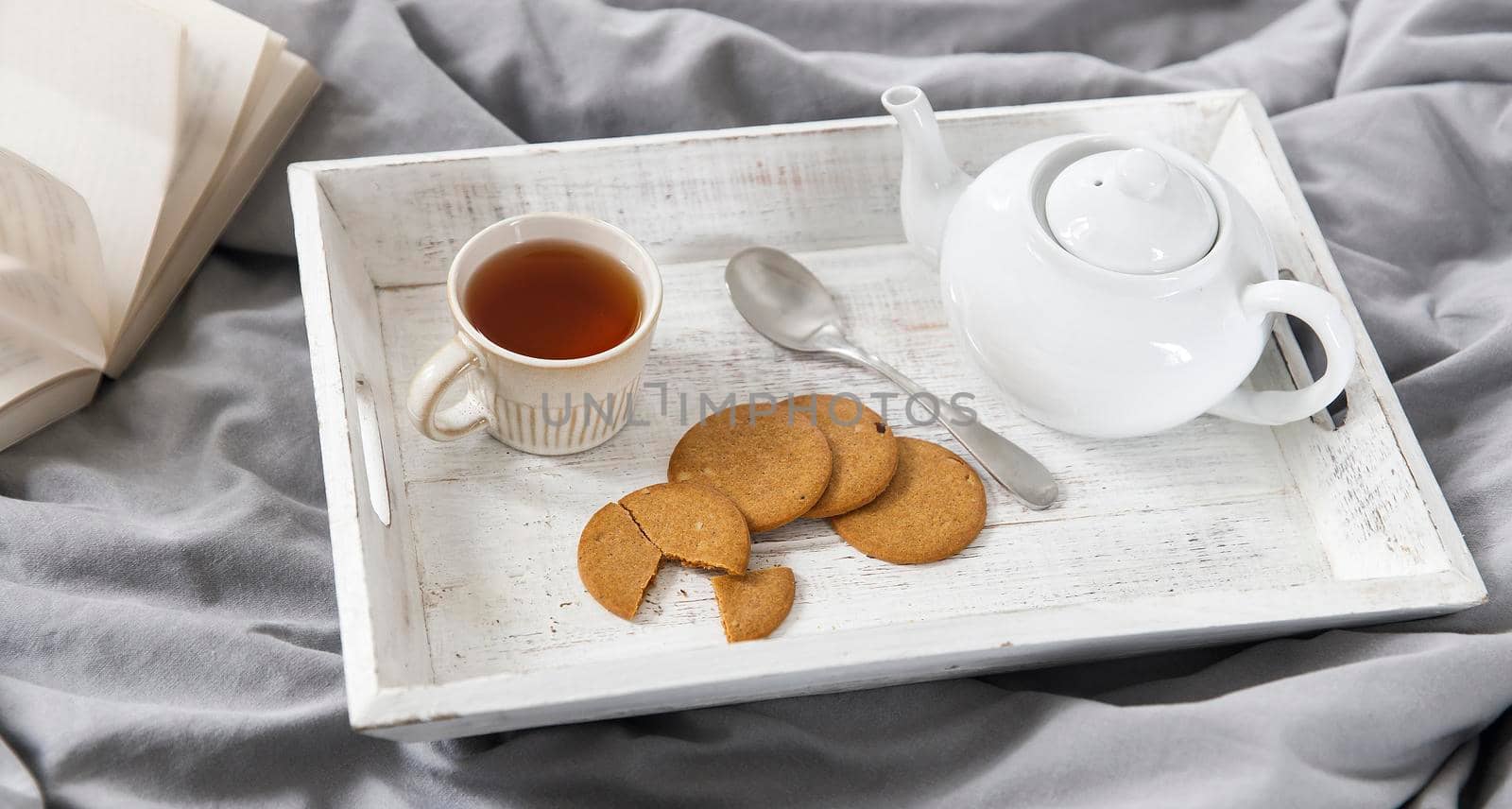 interior and home coziness concept. Top view. A cup of tea, a teapot with herbal tea, sugar bowl on a wooden tray on the bed. Porcelain cup