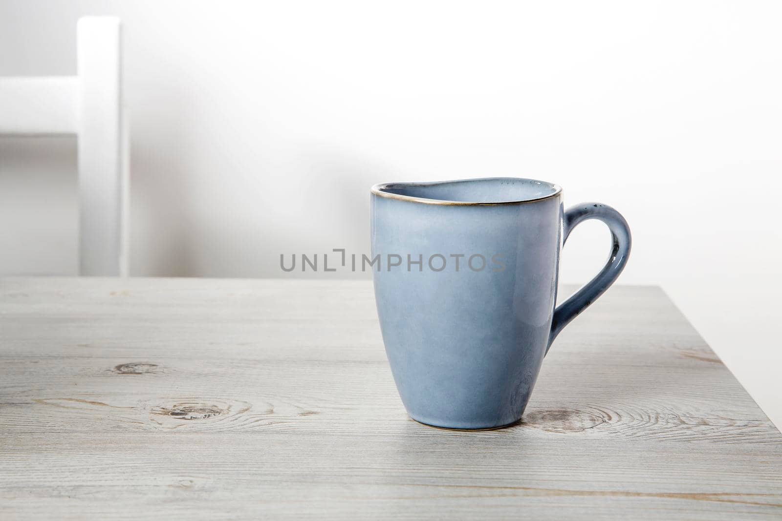 A blue ceramic cup on a beige table against a white wall. Place for text. Copy space by elenarostunova