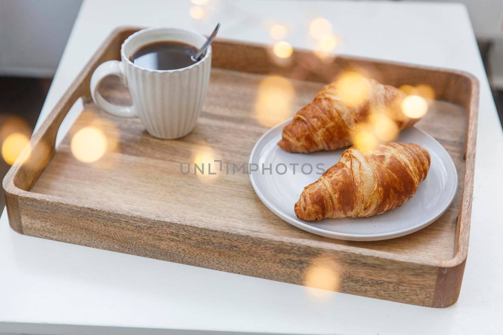 Freshly baked croissant on a gray round plate, white cup with coffee and garland on a tray on the table