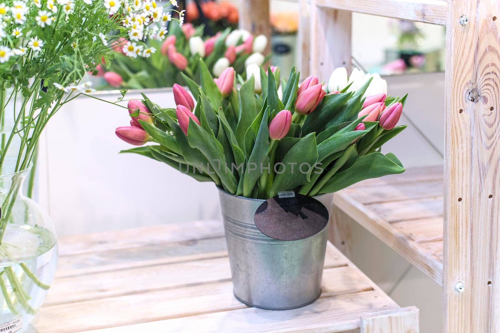 Bouquets of white and red tulips and daisies in a steel bucket for sale in a flower shop. by elenarostunova