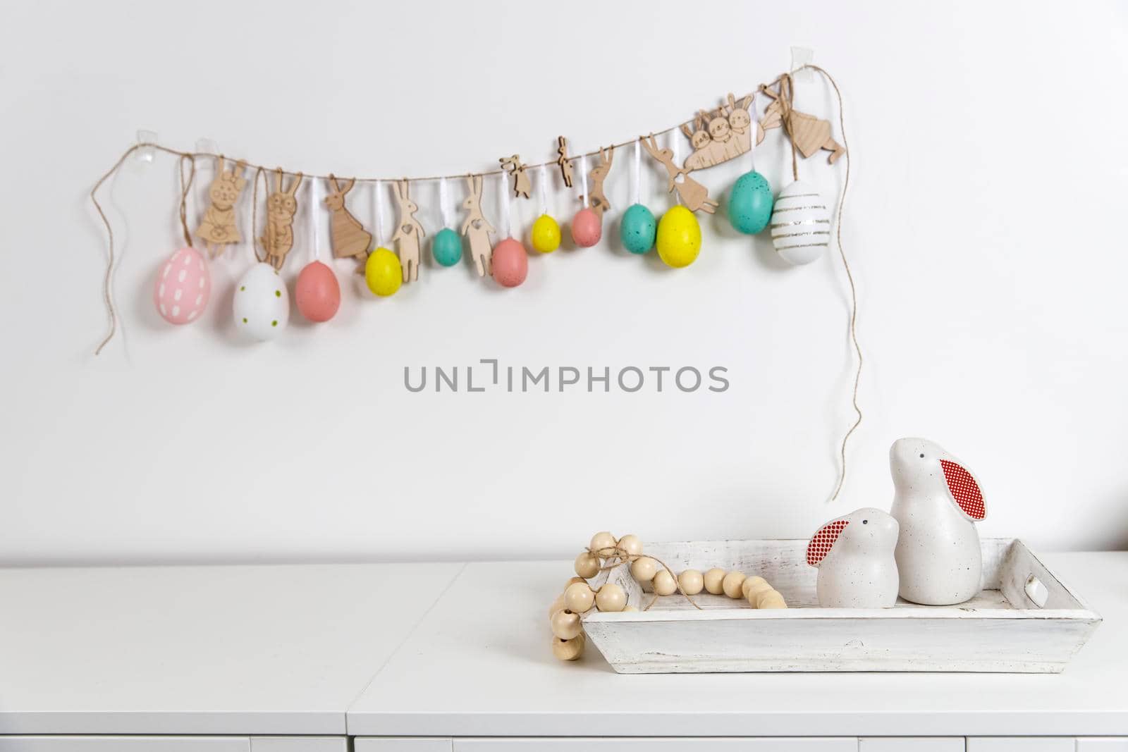 Fragment of the interior. Decorated children's room for Easter. A garland of plastic eggs on the wall. Ceramic rabbits and wooden cubes on the table. Place for your text. Easter card.