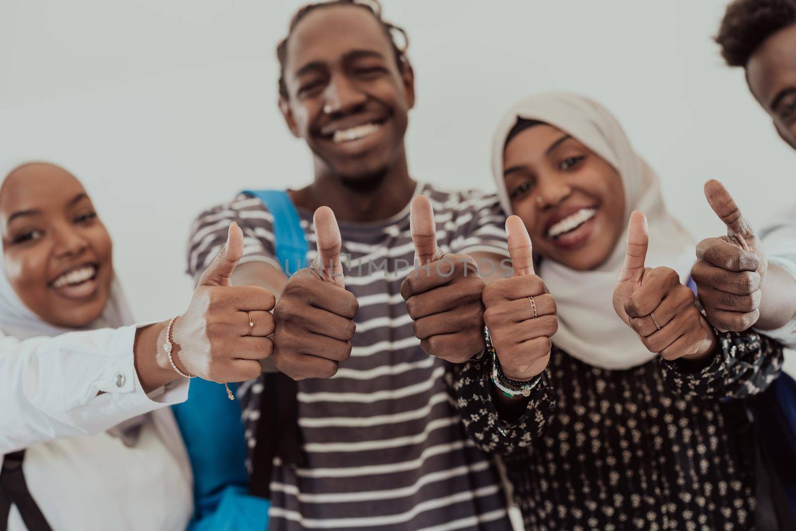 Group portrait of happy African students standing together against a white background and showing ok sign thumbs up girls wearing traditional Sudan Muslim hijab fashion. High-quality photo