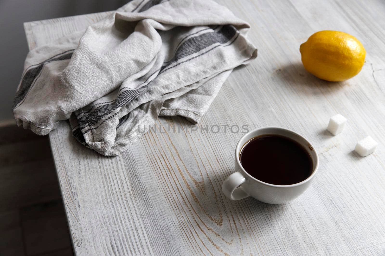 A cup of coffee, two pieces of sugar, a lemon on the table.