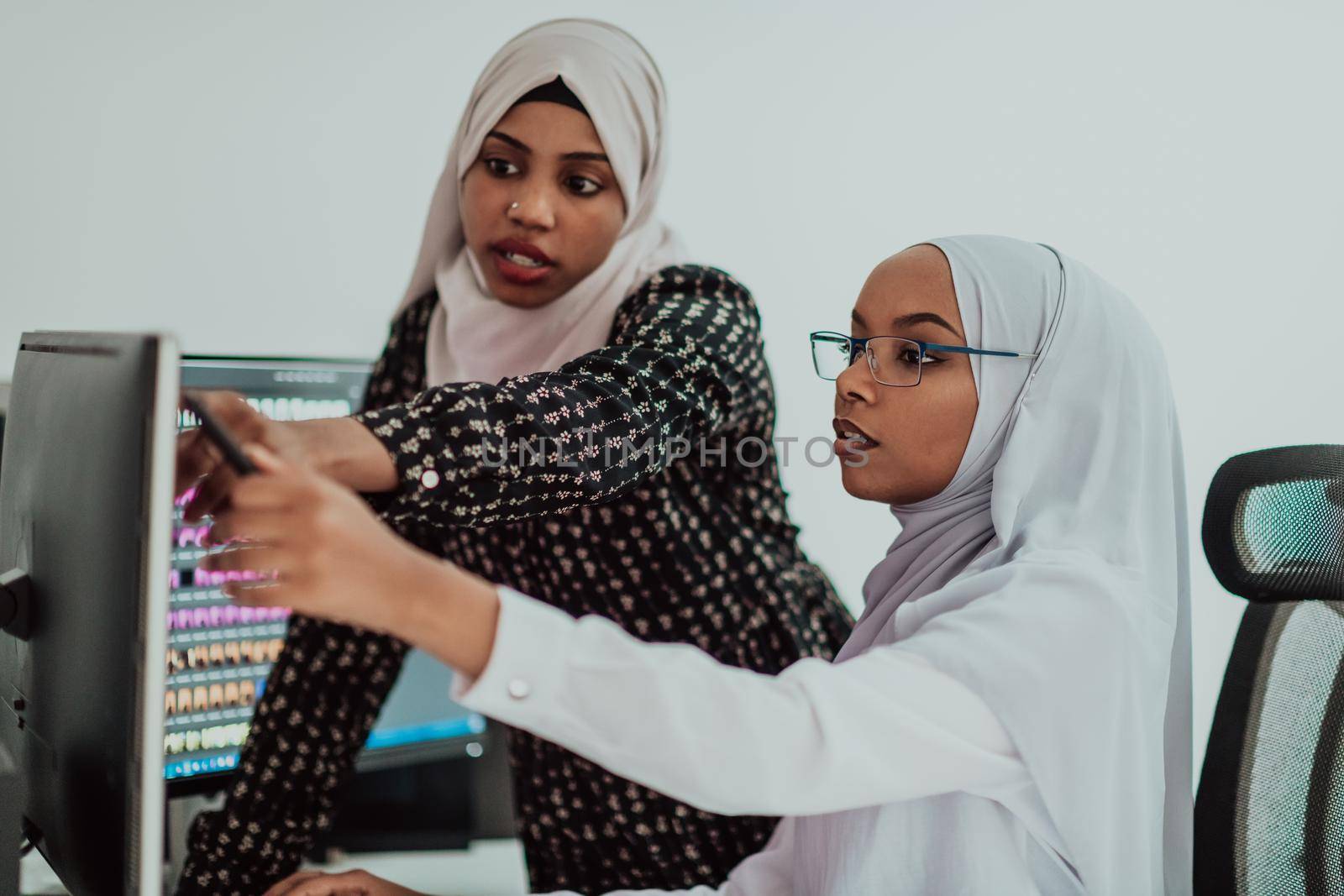 Friends at the office are two young Afro-American modern Muslim businesswomen wearing scarfs in a creative bright office workplace with a big screen. High-quality photo