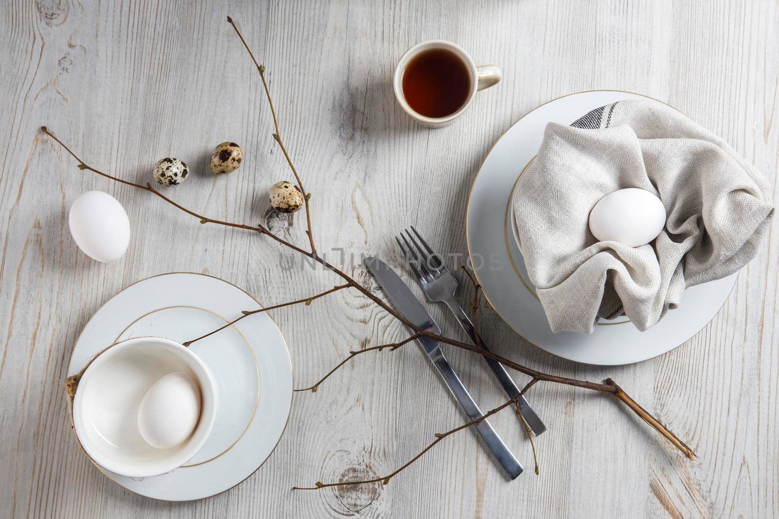 Table setting and decoration for Easter. White and partridge eggs in a plate with a napkin. poplar unblown branch