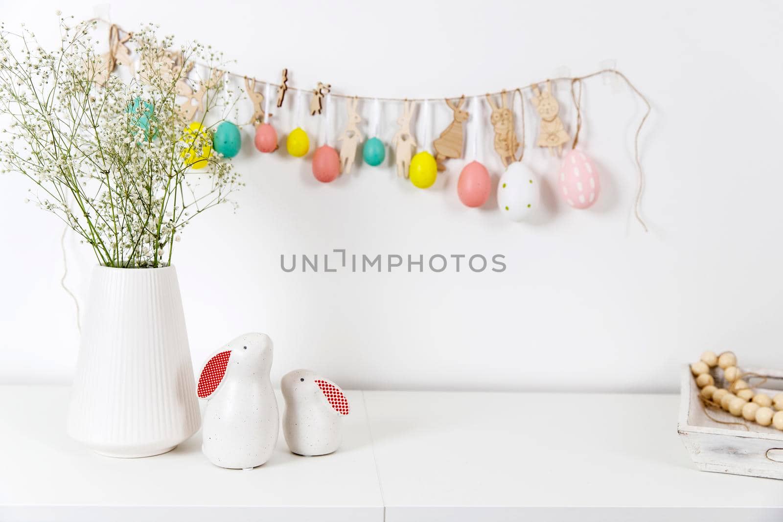 Fragment of the interior. Decorated children's room for Easter. A garland of plastic eggs on the wall. Ceramic rabbits and wooden cubes on the table. Place for your text. Easter card. by elenarostunova