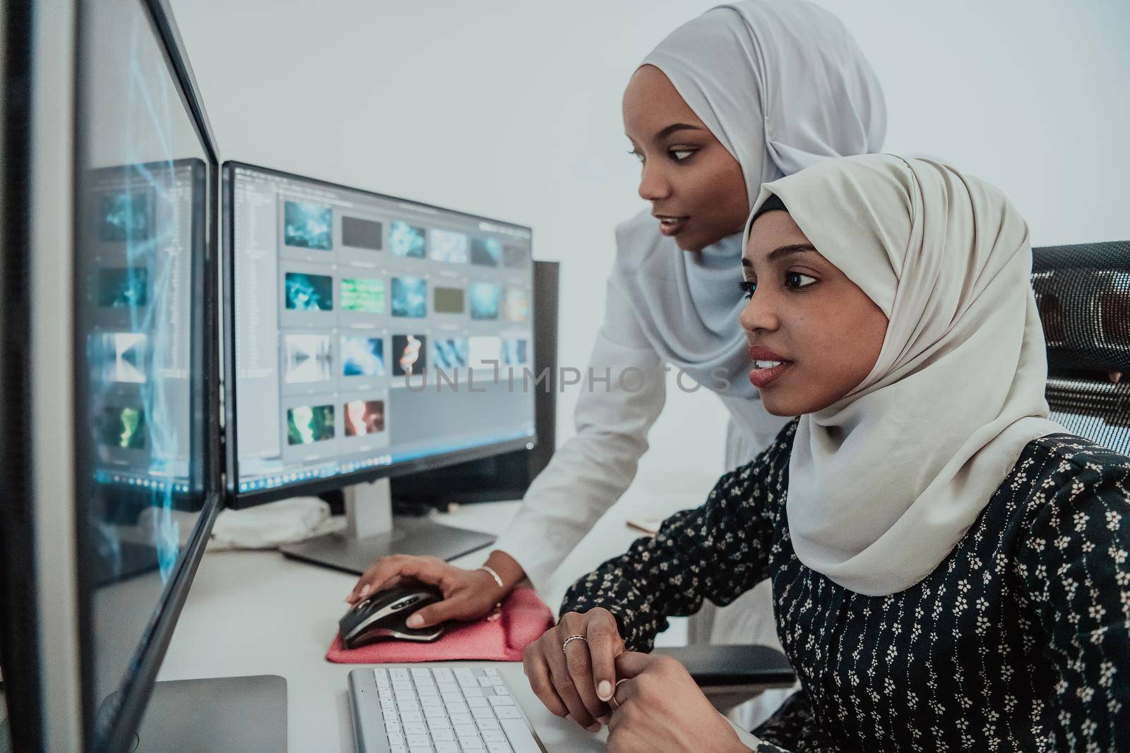 Friends at the office are two young Afro-American modern Muslim businesswomen wearing scarfs in a creative bright office workplace with a big screen. High-quality photo